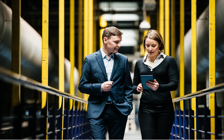 A woman in a factory wearing business attire and working on a tablet computer