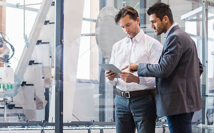 Two men in a factory wearing casual business attire and collaborating on a tablet computer